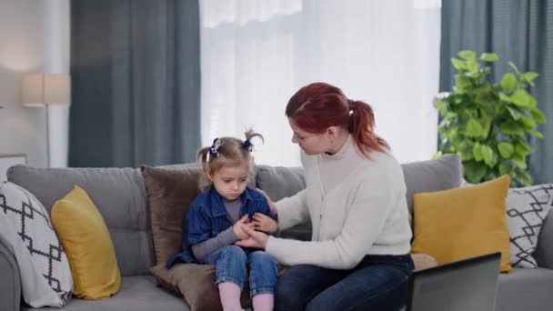 思いやりのある母親慰め少し不健康な娘ストローク彼女の頭をチェックしながら子供の温度居心地の良い部屋でソファに座って — ストック動画