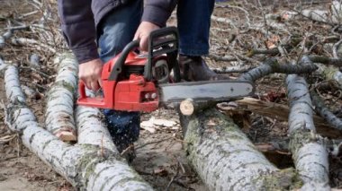 Oduncu, elektrikli testereli yaşlı bir adam dışarıda odun kesiyor.