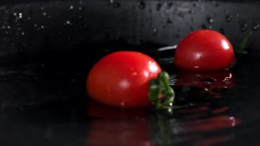Olgun taze vişneli domatesler koyu bir tabağa düşer. Su etrafa saçılır, yakın çekim.