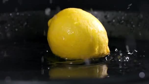 エキゾチックな果物 熟した黄色のレモンが暗い背景に水のプレートに落ち 水が側面に散布され クローズアップ — ストック動画