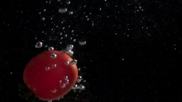 熟した野菜ジューシーなトマトは暗い背景に気泡のある水に落ち — ストック動画
