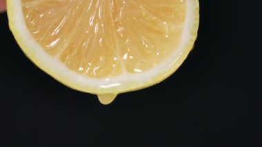 Lezzetli limon, bir damla su ya da meyve suyu koyu bir arka planda bir dilim limondan aşağı akar, yakın plan.