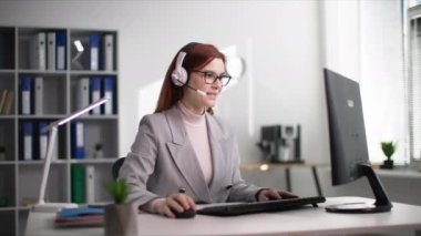 Teknik destek, çekici kadın ofiste bilgisayar başında otururken iletişim kulaklığı kullanarak bir müşteriyle iletişim kuruyor.