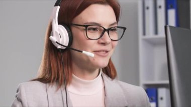 Gözlüklü genç bir kadının portresi çağrı merkezinde çalışırken kulaklık takan bir müşteriyle telefonda konuşuyor, gülümsüyor ve kameraya bakıyor.