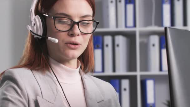 오퍼레이터 안경을 여성의 초상화 컴퓨터에서 작업하는 헤드셋을 사용하여 이야기하는 클로즈업 — 비디오