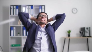 Neşeli Afro-Amerikan erkek çağrı merkezi çalışanı ofiste çalıştıktan sonra elleri başının arkasında oturmaktan zevk alıyor.