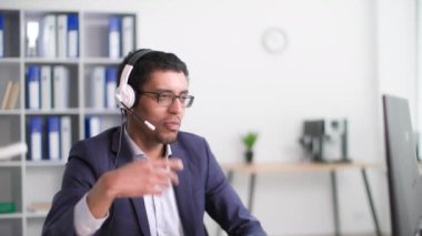 Teknik destek, gülümseyen Afro-Amerikan erkek çağrı merkezi çalışanı ofiste bilgisayar başında otururken kulaklıkla müşteriyle konuşuyor.
