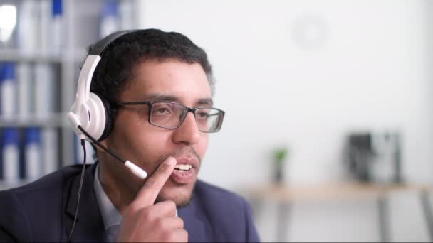 成功したアフリカ系アメリカ人実業家は オフィスに座っている間にコンピュータで働き ヘッドフォンでマイクを使って顧客と話をしながら 良いアイデアを喜びます — ストック動画