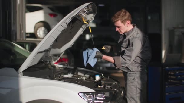車のサービス 特別な服の若いプロの男性整備士は 技術的な駅で自動車エンジンのオイルをチェックします — ストック動画