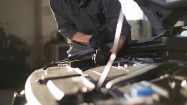 Otomobil servisi, üniformalı genç adam ellerinde bir aletle istasyonda açık kaputun yakınındaki araba motorunu kontrol ediyor.