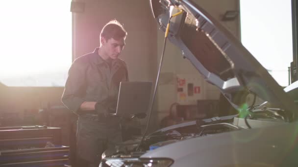 太陽光を背景に車のフードの下で手の中のツールと制服を着たプロの男の修理 — ストック動画