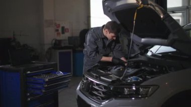 servis aracı, üniformalı genç erkek tamirci, teknik istasyonda arabanın kaputunun altındaki motoru kontrol ediyor.