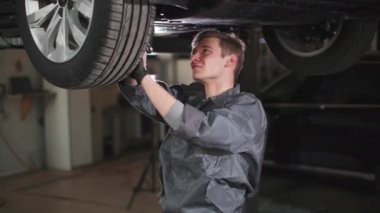 Otomobil merkezinde hidrolik rampada servis yapan, gülümseyen ve kameraya bakan genç otomobil tamircisinin portresi.