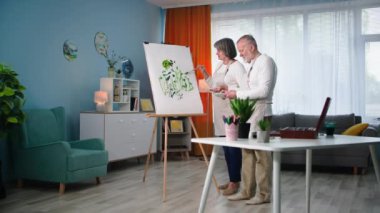 Yaratıcılık emekliye ayrıldı, fırça ve boya kullanan yaratıcı yaşlı kadın ve erkek rahat bir odada resim sehpasıyla tuvale modern bir resim çiziyor.