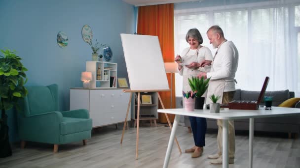 現代の年金受給者は引退で創造的な絵を描くのが好きで 女性と一緒に家でブラシとペンキで絵を描く — ストック動画