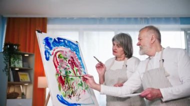 Yaratıcı emekliler, fırça ve boya kullanan yetenekli yaşlı erkek ve kadın oturma odasında sehpası olan tuvale modern bir resim çizerler.