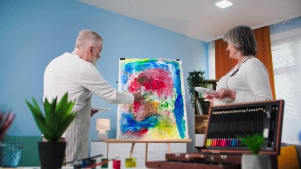 現代の趣味で創造的な高齢者の女性と男性は自宅でキャンバスにブラシや塗料を使用して絵を描くのが好きです — ストック動画