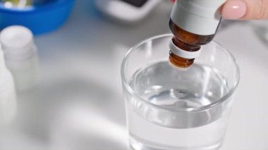 Kendini kötü hisseden kadın, kendini iyi hissetmek için şişeden damla damlatıcısı damlatarak şeffaf bir bardak suya dönüşür.