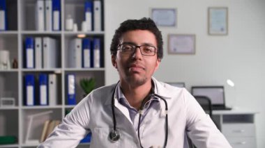 Uzaklık tıbbı, gözlüklü genç siyahi bir doktor bilgisayardaki bir video bağlantısıyla hastayla iletişim kuruyor ve kameraya bakıyor.
