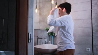 Tatlı erkek çocuk sabah rutinini lavabonun yanında yapıyor, su tedavisinden sonra yüzünü havluyla silerek aynaya bakıyor.