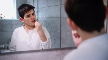 Diş macunu ve fırçayla dişlerini fırçalayıp banyonun aynasına bakan sevimli bir çocuğun portresi.