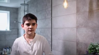 Erkek çocuk banyoda aynaya bakarak dişlerini eko bambu fırçasıyla fırçalıyor.