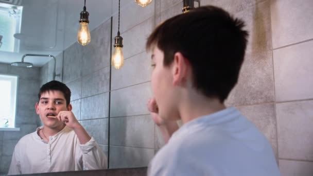 사랑스러운 소년은 대나무 칫솔로 치아를 화장실에서 거울을보고 넣습니다 — 비디오