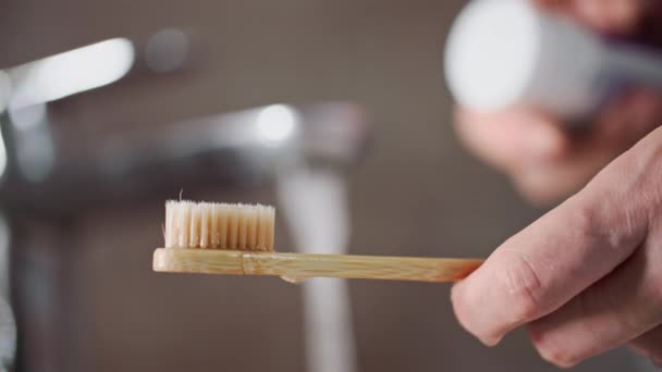 個人的な衛生 ティーンエイジャーはタップで水をオンにし 洗面台の竹の歯ブラシの背景に歯磨き粉を塗ります クローズアップ — ストック動画