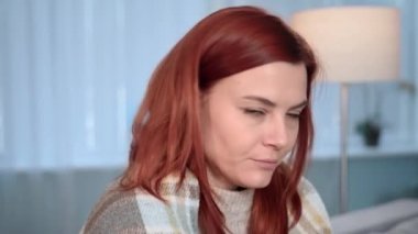 Çekici bir kadının evde üşüttüğü portresi ellerini ısıtıyor ve kanepede oturmuş kameraya bakarken sıcak bir battaniye giyiyor.