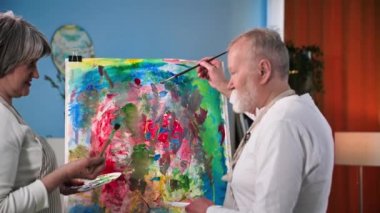 Emekli hobi, yetenekli erkek ve kadın yaşlılar tuvale resim çizerler. Rahat bir odada boya ve fırçayla birlikte.