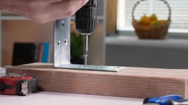 Katılımcı, erkek işçi tornavida ve matkap kullanarak metal bir köşeyi ahşap bir rafa vidaladı.
