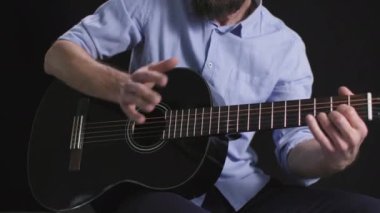 Bir enstrüman çalıyor, erkek bir müzisyen karanlık bir arka planda gitar çalıyor.