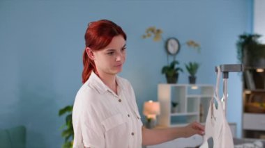 Ev aletleri, modern bir buhar makinesi kullanan kadın ev hanımı odada bir tişört ütülüyor.