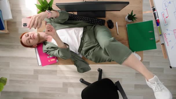 在工作场所休息 年轻女人一边吃午饭一边滚动手机 躺在办公室的桌面上 — 图库视频影像