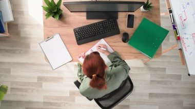 İş akışı, genç bir kadın not defterine not alır ve ofiste bilgisayar başında çalışırken eline bir cep telefonu alır.