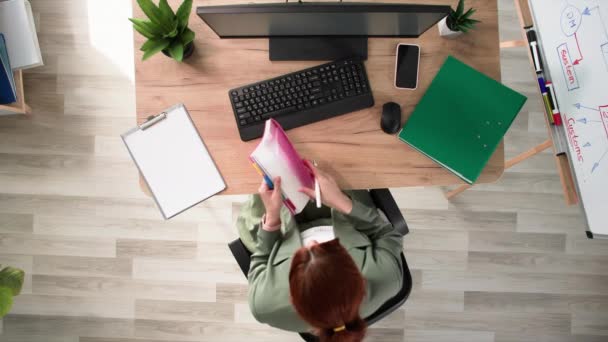 働く日 オフィスで働く女性の従業員はオフィスのコンピュータで座っている間ノートでノートを作ります 上の眺め — ストック動画