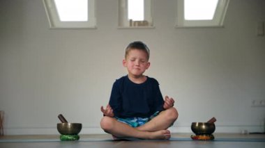 Kapalı gözlü erkek çocuk, karemat üzerinde nilüfer pozisyonunda otururken Tibet müzik kaseleri arasında medecia sırasında.