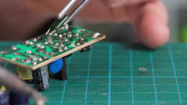 Erkek elektronik mühendisi lehim demiri kullanarak elektronik kontrol panelini tamir ediyor, yakın plan.
