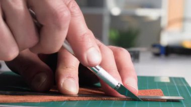 El işi, dikiş aletleri kullanan bir adam masa üzerinde bir ürün yapmak için bir parça deri keser.