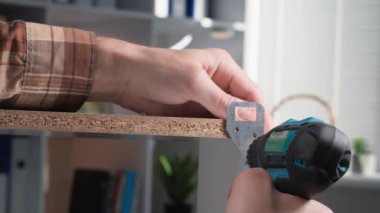 Mobilya topluyor, tornavida kullanan bir adam metal bir köşeyi tahta bir rafa vidalıyor, yakın plan.