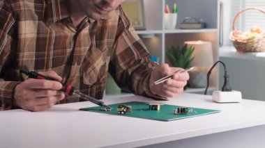 Levye kullanan bir adam evdeki bir masada mikro devreleri tamir ediyor.