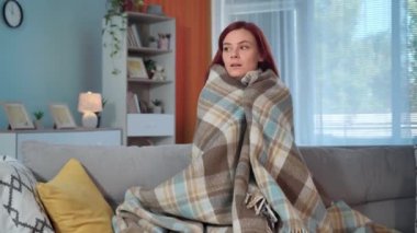 Ekoseli genç bir kadın evdeki soğuk bir odada, bir kanepede oturuyor.