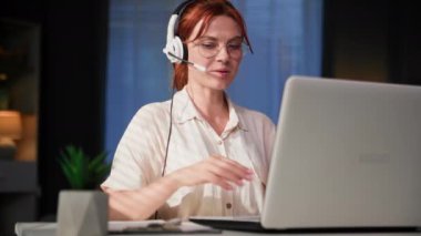 Çağrı merkezi operatörü, mikrofonlu ve monitörlü genç bir kadın müşterisiyle masada otururken bilgisayar üzerinden iletişim kuruyor.