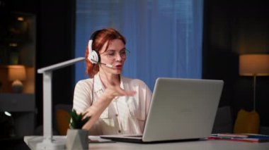 Ev ofisi, sevimli genç kadın çağrı merkezinde uzaktan çalışıyor ve odada otururken video bağlantısı üzerinden kulaklıkla konuşuyor.