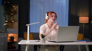 Serbest meslek, kulaklıklı genç bir kadın evde oturmuş kameraya bakıp gülümserken uzaktan video iletişimiyle patronuyla konuşuyor.