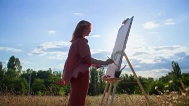 Hobi olarak, genç bir kadın, güneşli bir günde sehpada boya ve fırçalarla resim çizer.