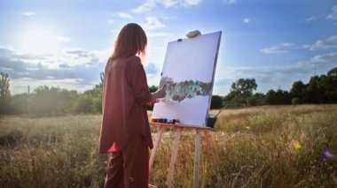 Yetenekli genç kadın resim yapmayı sever ve arka planda güneş ışınları üzerine yaratıcı bir resim çizer.