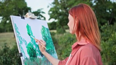 Sanat terapisi, genç kadın ressam bir resim çizer boya sehpası kullanır ve tarladaki güneş ışınlarının arka planlarını tarar.