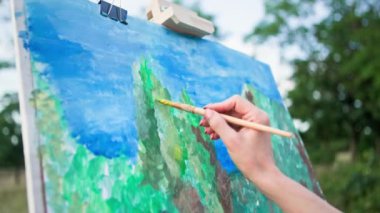 Çağdaş sanat, genç kadın ressam açık havada bir resim çizer ve fırçalar, kadın eli yakın çekim.