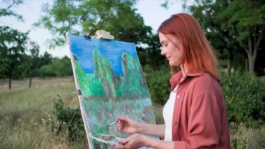 En sevdiği meşgale, yetenekli bir kadın sanatçı yeşil ağaçların arka planında dururken resim çizer ve fırçalarla resim yapar.